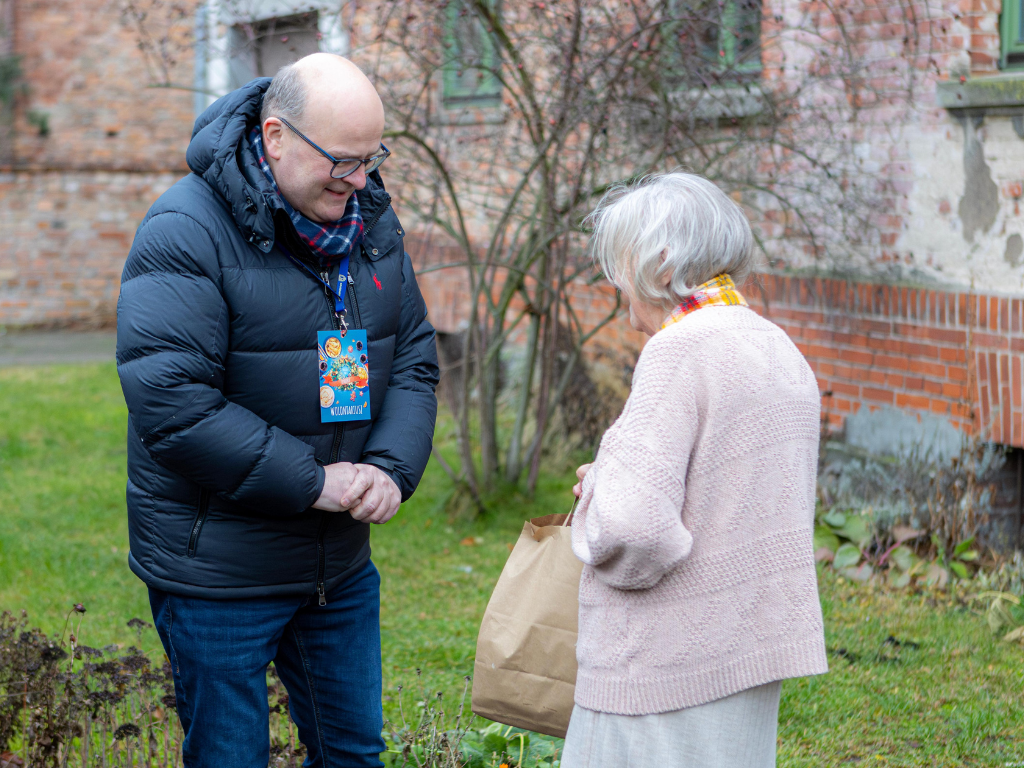 Fotografia przedstawia prezydenta Grudziądza przekazującego świąteczną paczkę seniorce. 