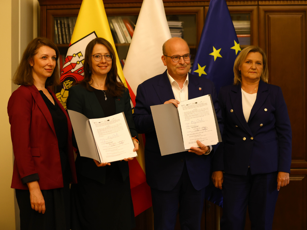 Na zdjęciu na tle flag stoją od lewej strony: Katarzyna Kycia, ekspert ds. relacji regionu kujawsko-pomorskiego w Banku Gospodarstwa Krajowego, Katarzyna Bekisz, dyrektor rozwoju regionu kujawsko-pomorskiego w Banku Gospodarstwa Krajowego, Maciej Glamowski, prezydent Grudziądza oraz Małgorzata Kosińska, skarbnik miasta.